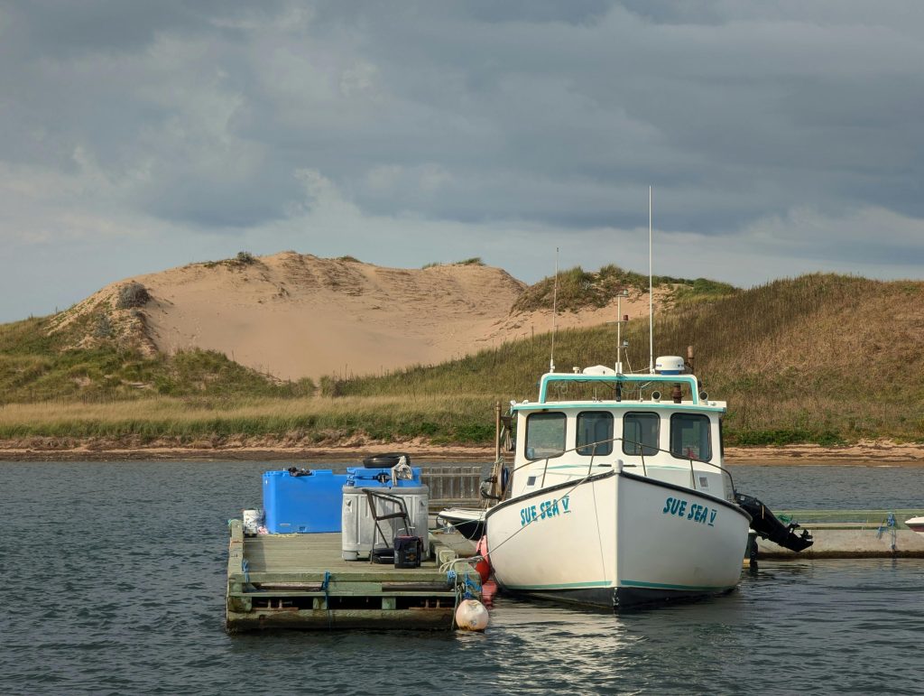 A fishing boat docked at Cape Breton Island, Nova Scotia, beside sand dunes.